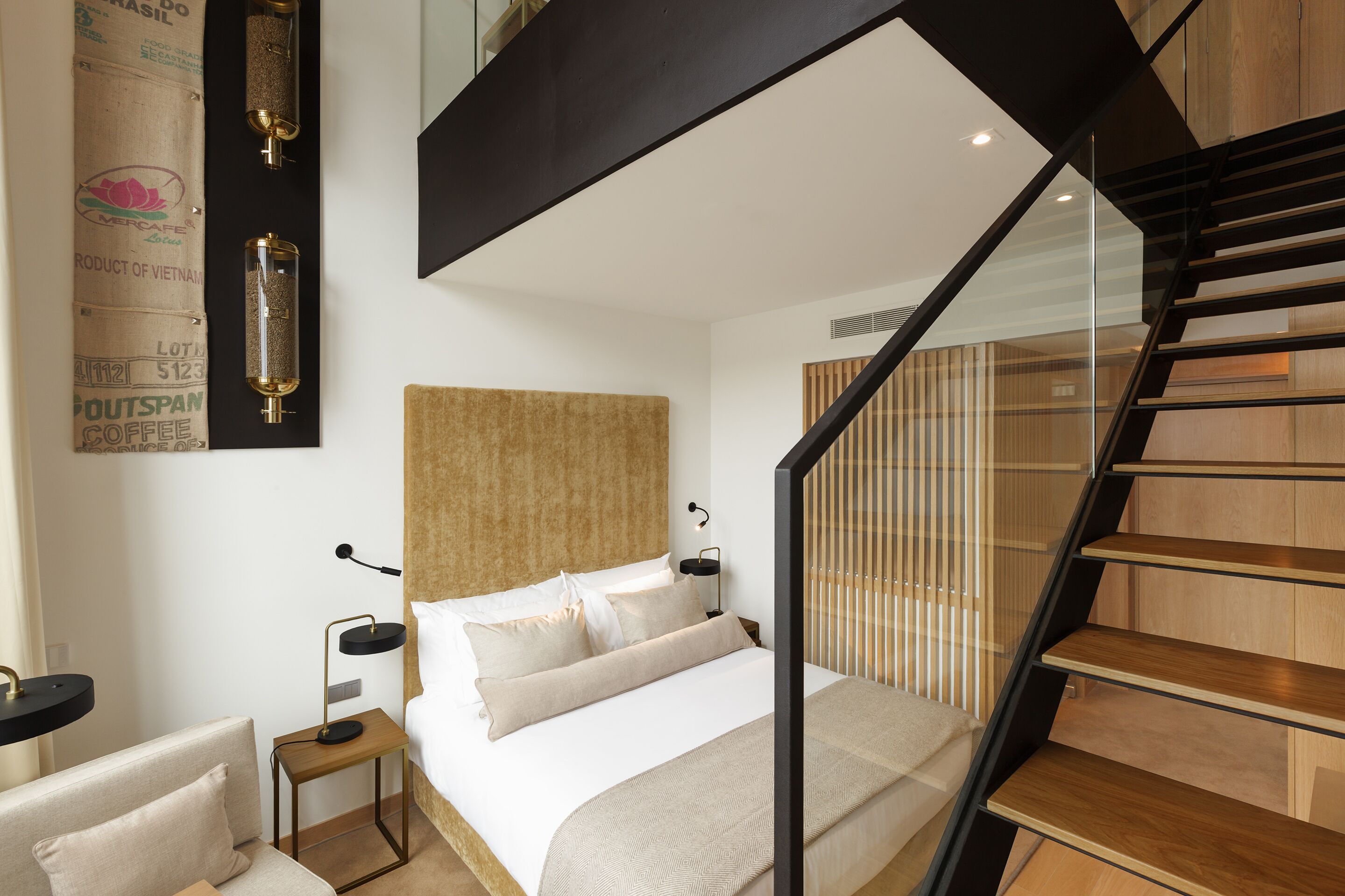 A modern bedroom with a large bed, a nightstand, a desk, and a staircase.