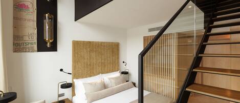 A modern bedroom with a large bed, a nightstand, a desk, and a staircase.