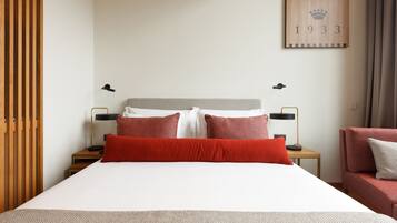 A neatly arranged hotel room with a large bed, two bedside tables, a red sofa, and a wall-mounted number sign.