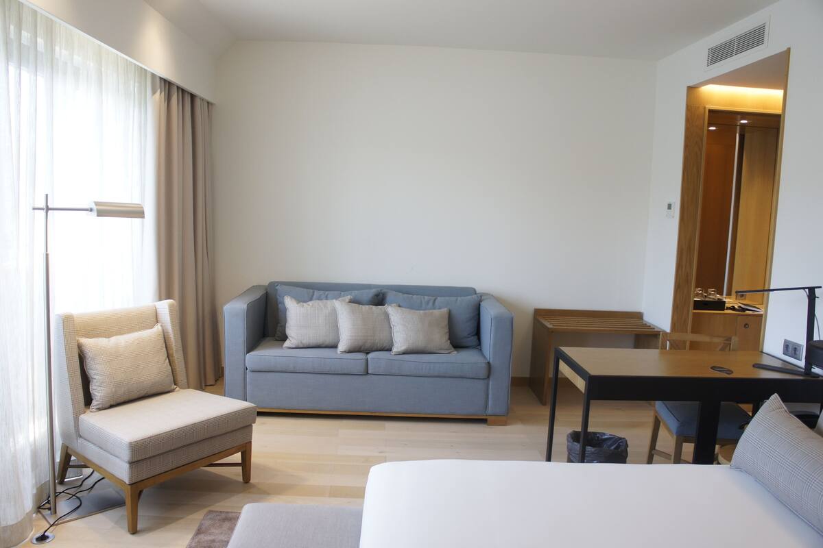 A modern hotel room with a sofa, a chair, a small table, and a bed.