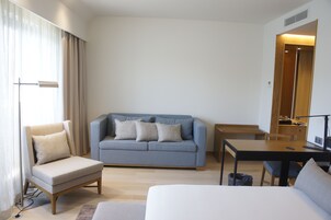 A modern hotel room with a sofa, a chair, a small table, and a bed.