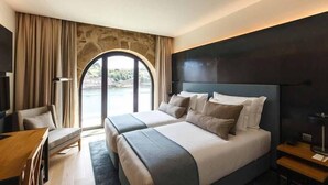 A modern hotel room with a large bed, a desk, and a view of a body of water through a large window. - Neya Porto Hotel (Porto)