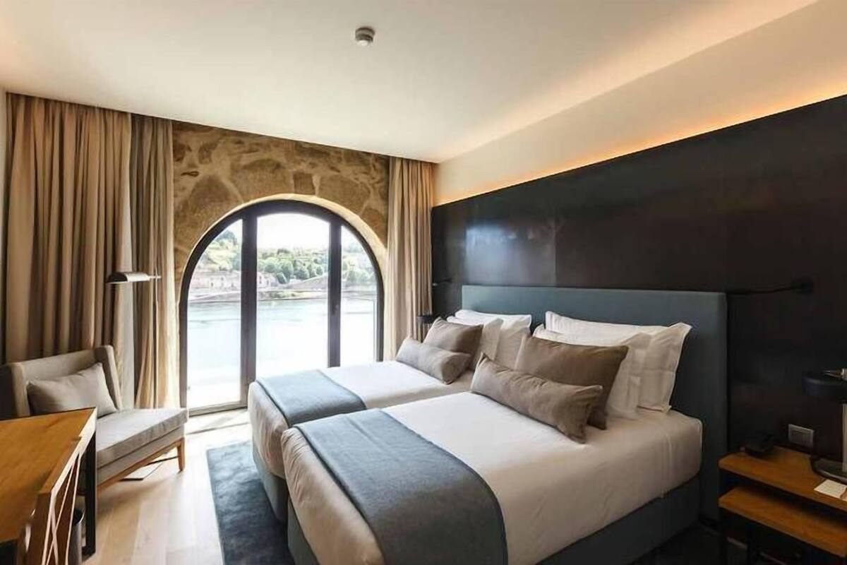 A modern hotel room with a large bed, a desk, and a view of a body of water through a large window.