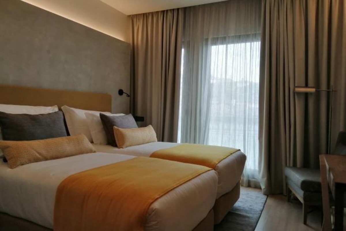 A hotel room with two beds, a desk, and a large window with curtains.