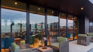 A modern outdoor seating area with glass walls, green and blue chairs, and a small table with a lamp. - Neya Porto Hotel (Porto)