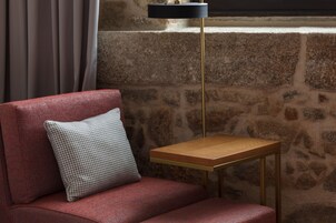 A red sofa with a checkered pillow, a small wooden table, and a stone wall in the background.