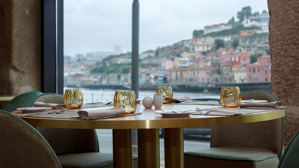 A dining table set with glasses, plates, and cutlery, overlooking a cityscape with buildings and a body of water. - Neya Porto Hotel (Porto)