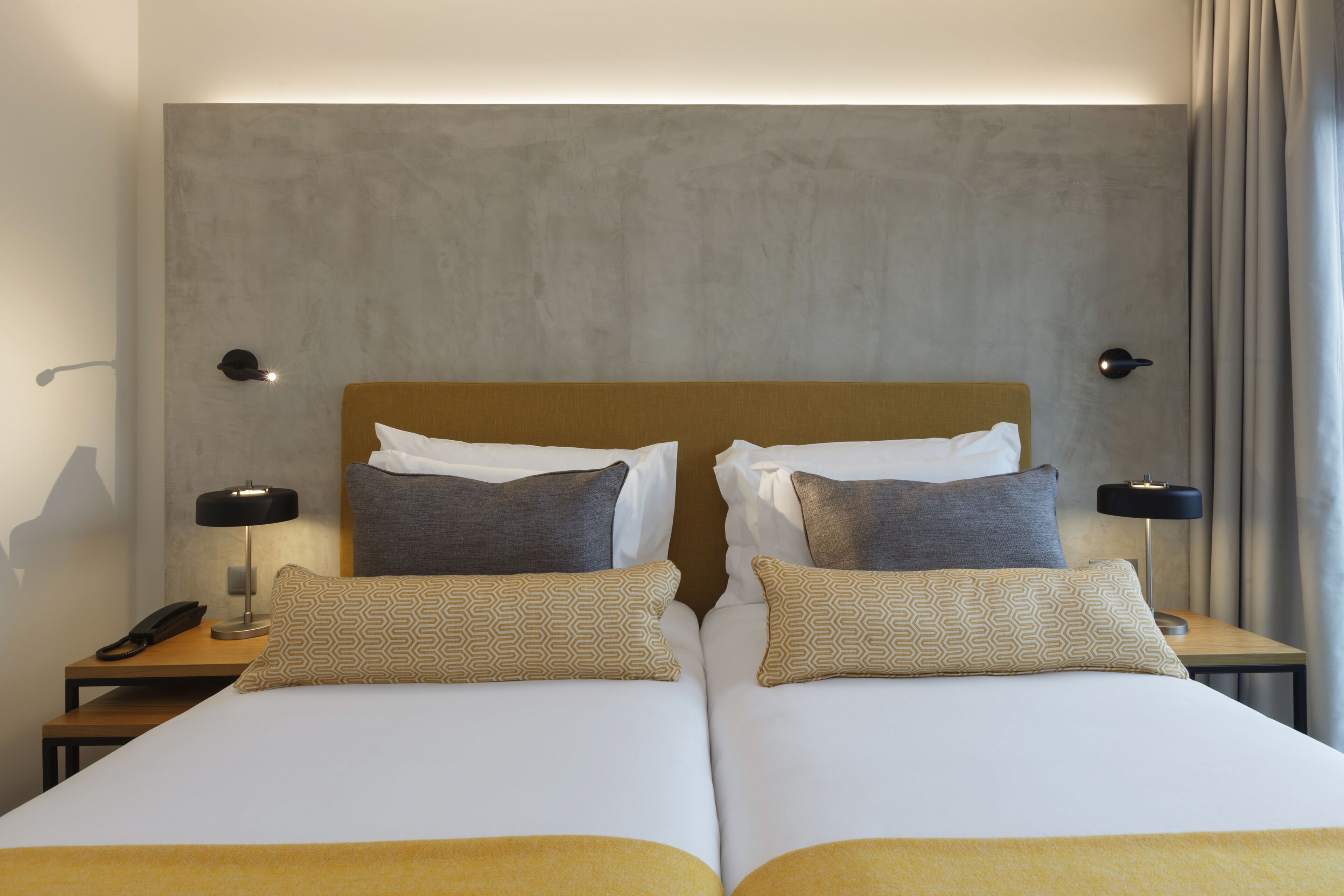 A hotel room with two beds, a grey textured headboard, bedside lamps, and a telephone on the nightstand.