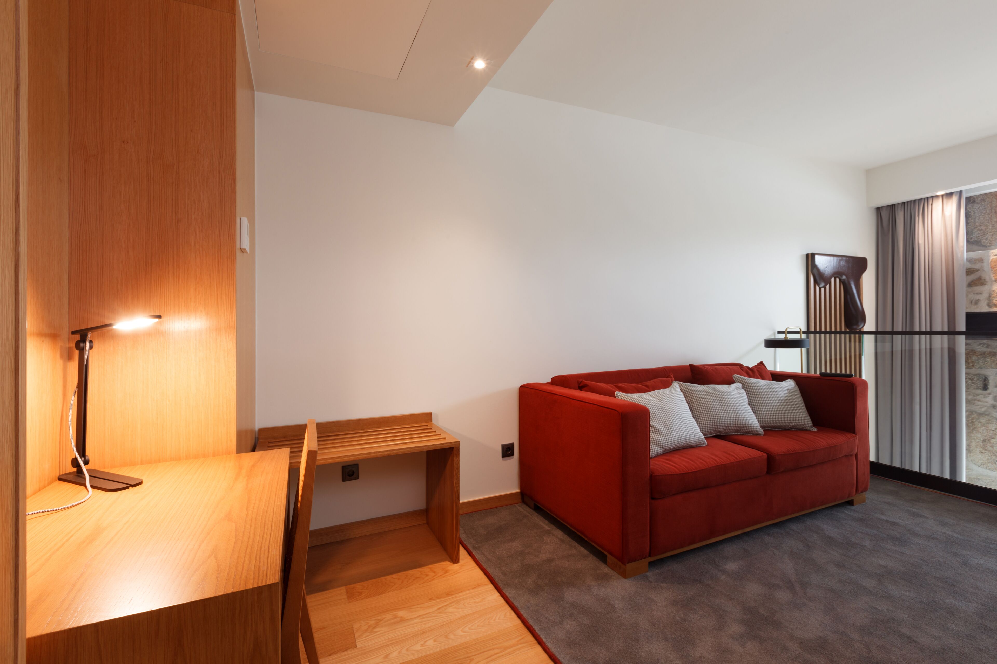 A modern living room with a red sofa, a wooden desk, and a lamp.