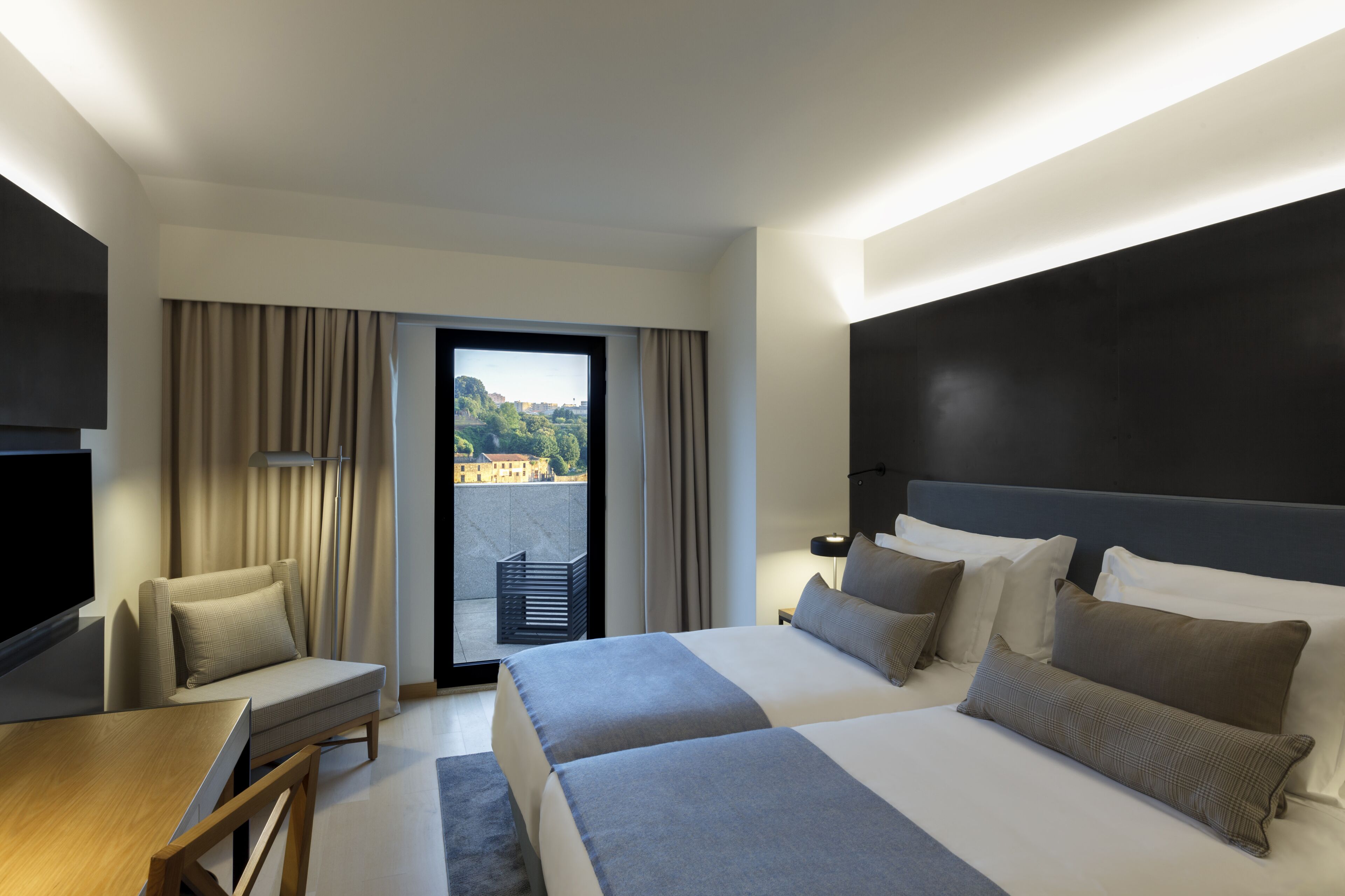 Quarto de hotel com uma cama grande, uma escrivaninha e vista para a cidade pela janela.