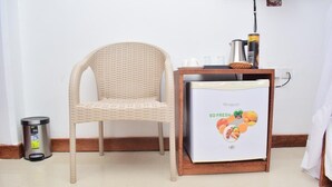 Una habitación con una silla de mimbre, un refrigerador pequeño que muestra productos frescos, un cesto de basura y un enchufe.