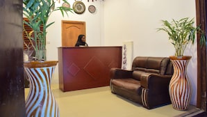Un área de recepción con un mostrador de madera, un sofá de cuero marrón y dos grandes jarrones a rayas con plantas.