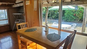 Een houten interieur met een tafel en stoelen, een raam met een parasol erbuiten, en een houten plafond.