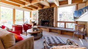A cozy living room with a stone fireplace, wooden beams, and large windows. - Treetops Condo Short Walk to Base of Eagle Bahn Gondola by RedAwning (Vail)