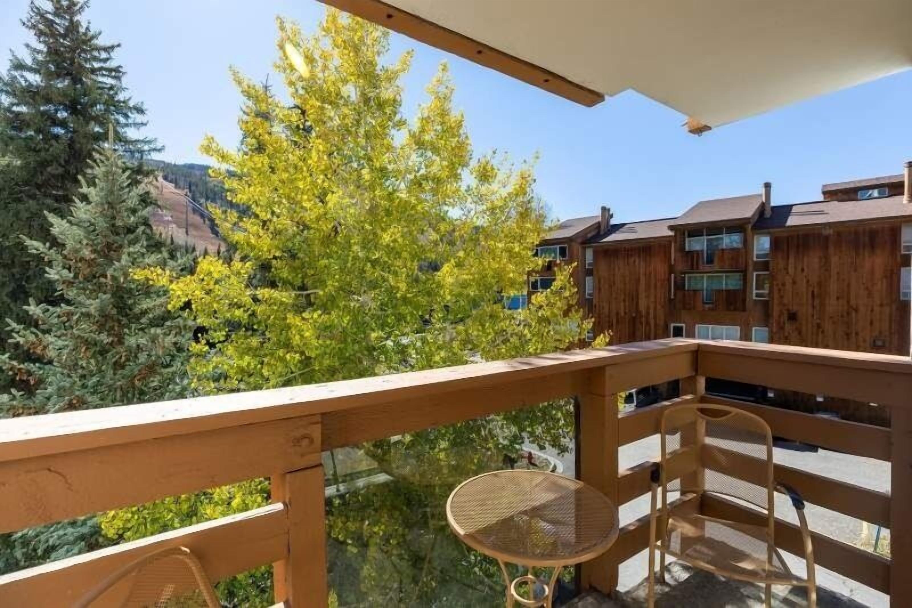 Un balcón de madera con vista a árboles y un edificio al fondo.