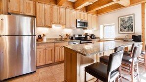 A modern kitchen with wooden cabinets, stainless steel appliances, and a central island with bar stools. - Treetops Condo Short Walk to Base of Eagle Bahn Gondola by RedAwning (Vail)