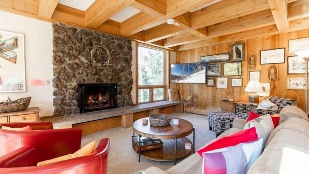 A cozy living room with a stone fireplace, wooden beams, and a large window. - Treetops Condo Short Walk to Base of Eagle Bahn Gondola by RedAwning (Vail)