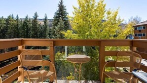 A balcony with wooden railings, two wicker chairs, and a small round table. - Treetops Condo Short Walk to Base of Eagle Bahn Gondola by RedAwning (Vail)