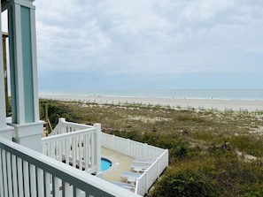 A beach view from a balcony with a pool and lounge chairs.