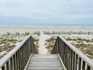 A wooden boardwalk leading to a sandy beach with a clear view of the ocean.