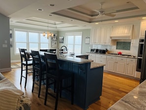 A kitchen with a central island, bar stools, a large window, and a ceiling fan. - 287 Obw 6 Bedroom Home by RedAwning (Supply)