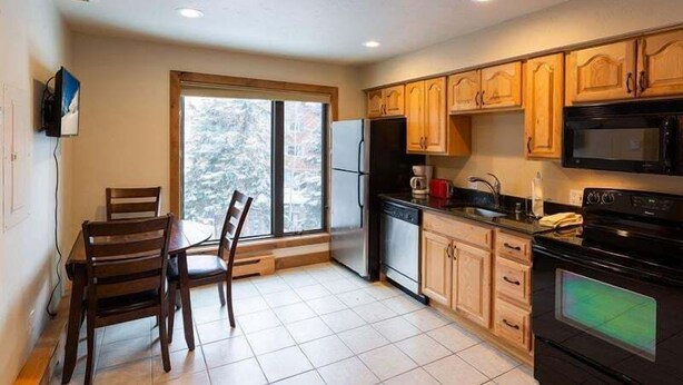 A kitchen with wooden cabinets, a refrigerator, a microwave, and a dining table with chairs. - Breakaway West Studio Condo with Pool and Hot Tubs by RedAwning (Vail)