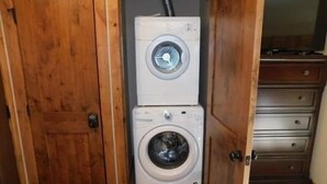 A compact laundry room with a stacked washer and dryer, wooden door, and a small cabinet. - Breakaway West Studio Condo with Pool and Hot Tubs by RedAwning (Vail)