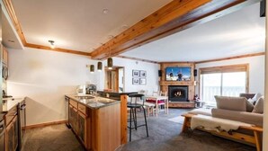 A cozy living room with a fireplace, stone flooring, wooden beams, and a bar area.