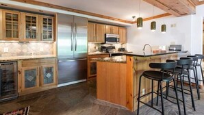 A kitchen with wooden cabinets, a stainless steel refrigerator, a microwave, and a bar area with stools.
