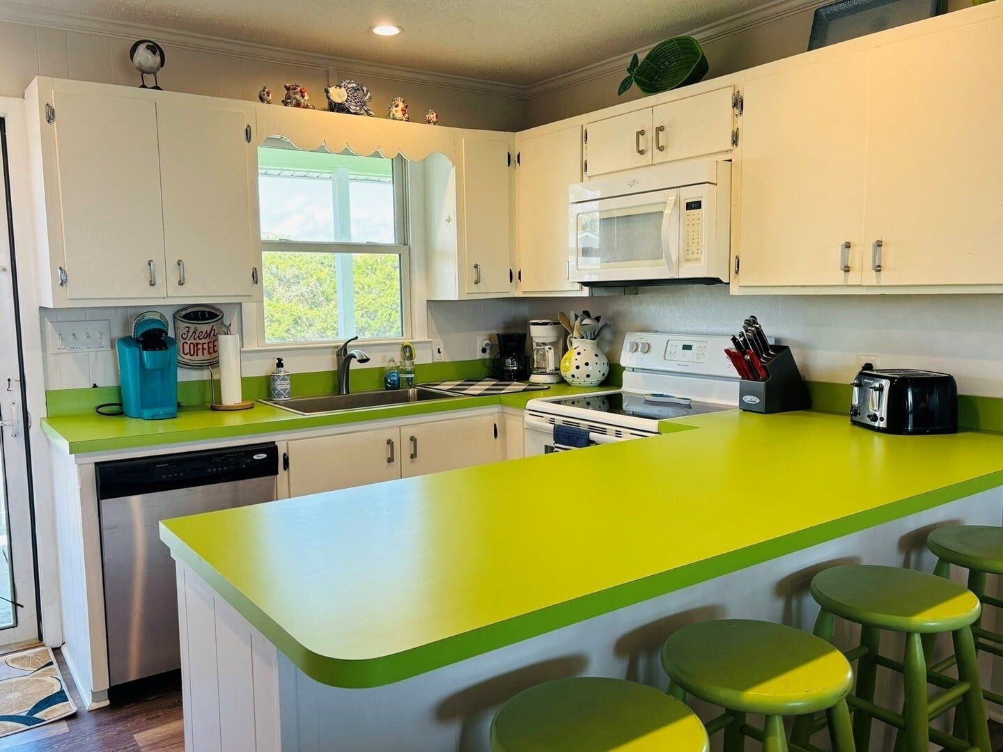 A kitchen with white cabinets, a green countertop, a microwave, a dishwasher, and a window.