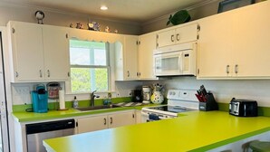 A kitchen with white cabinets, a green countertop, a microwave, a dishwasher, and a window. - Lime Inn 4 Bedroom Home by RedAwning (Supply)