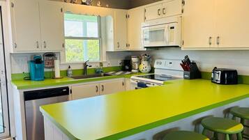 A kitchen with white cabinets, a green countertop, a microwave, a dishwasher, and a window.