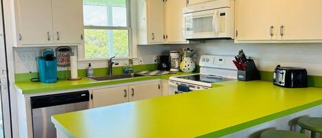A kitchen with white cabinets, a green countertop, a microwave, a dishwasher, and a window.
