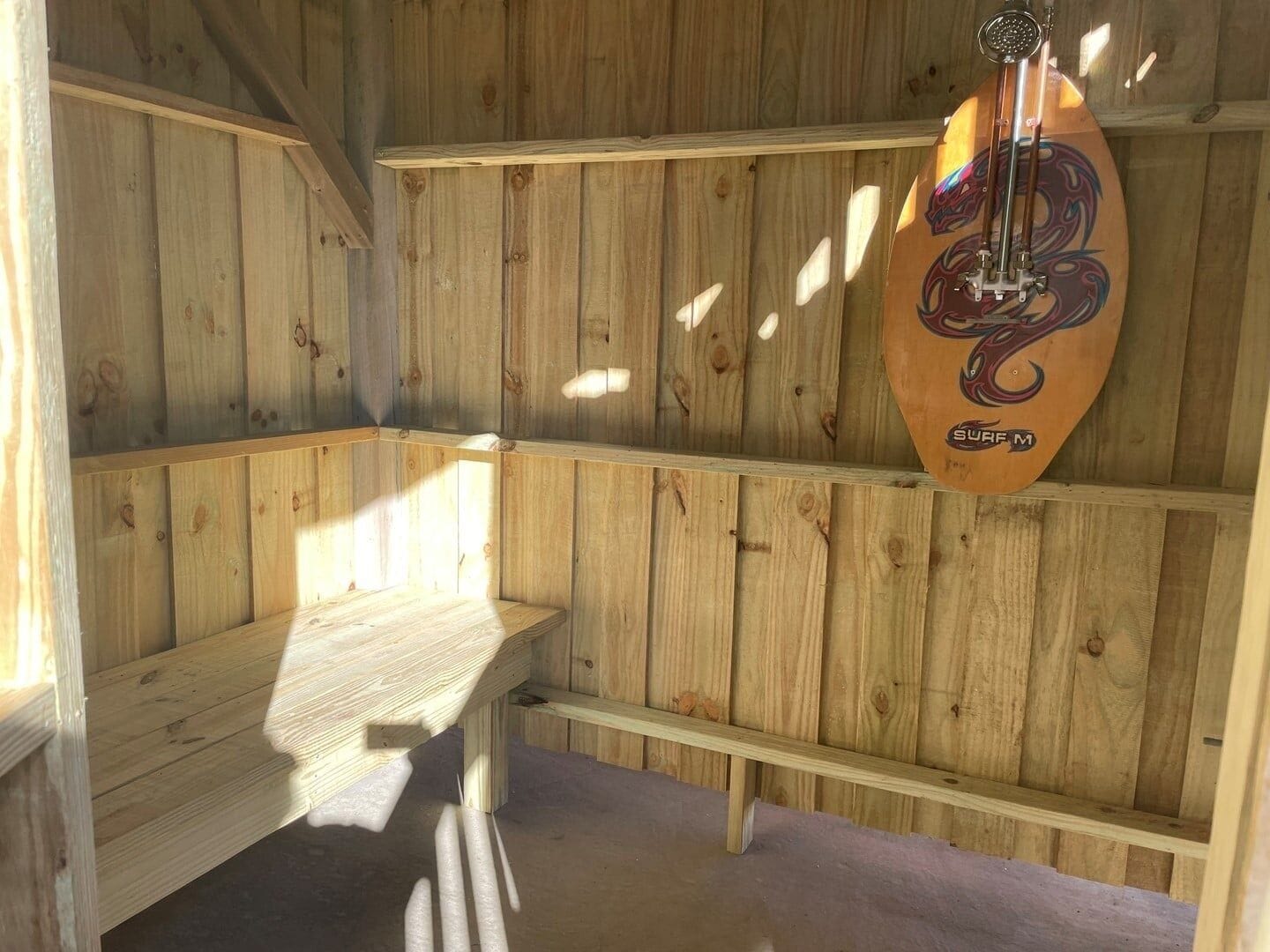 Una habitación de madera con un banco, una tabla de surf y una ducha.