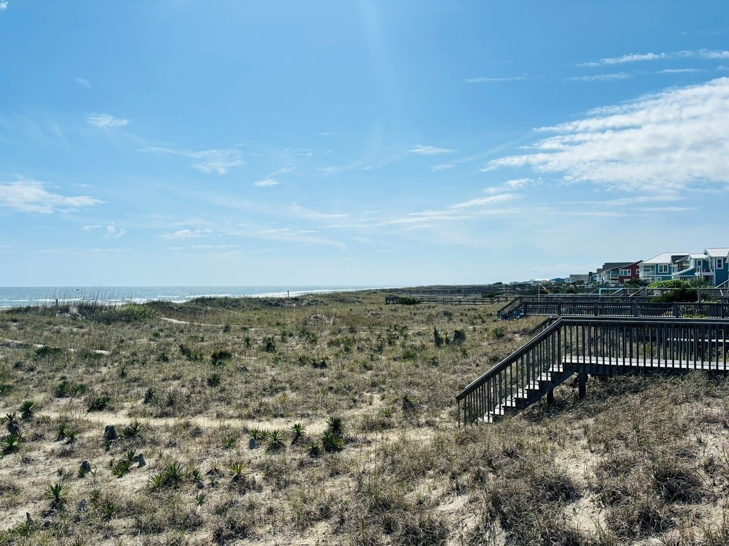 Un paysage côtier avec une plage de sable, une végétation clairsemée et un escalier menant à un quartier résidentiel avec des maisons.