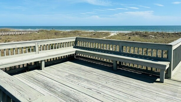 A wooden deck with a railing overlooking a beach. - Lime Inn 4 Bedroom Home by RedAwning (Supply)