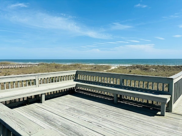 A wooden deck with a railing overlooking a beach.