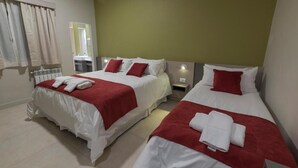 Une chambre d’hôtel avec deux lits, chacun agrémenté de draps blancs et de touches de couleur rouge, une petite table de chevet et une fenêtre avec des rideaux.