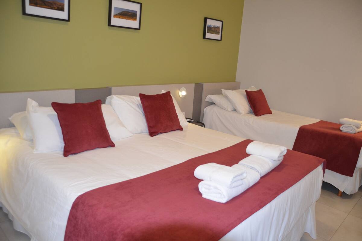 Une chambre d’hôtel avec deux lits, chacun agrémenté de draps blancs et de touches de couleur rouge. Des tableaux encadrés sont accrochés au mur au-dessus des lits.