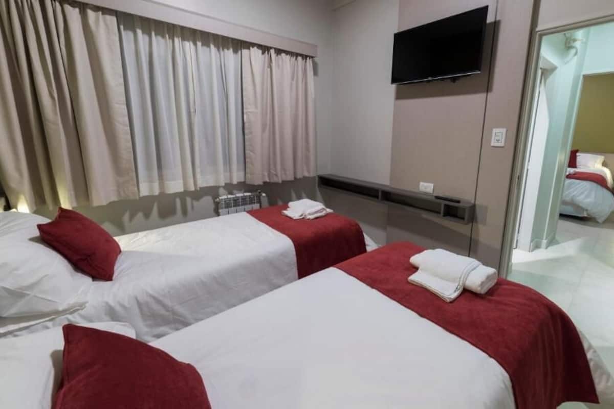 Une chambre d’hôtel avec deux lits, chacun étant équipé de draps blancs et d’oreillers rouges. Un téléviseur à écran plat est fixé au mur, au-dessus des lits.