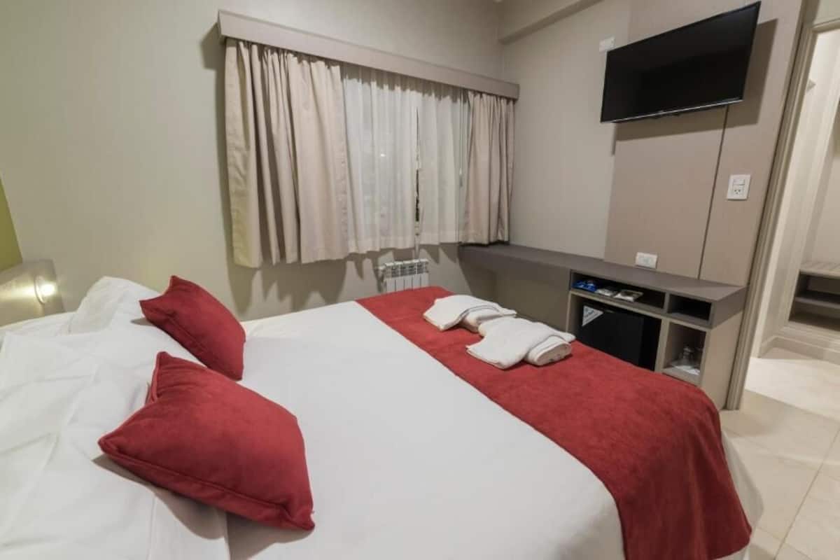 Une chambre d’hôtel avec un lit, des oreillers rouges, un téléviseur fixé au mur et un petit bureau avec un miroir.
