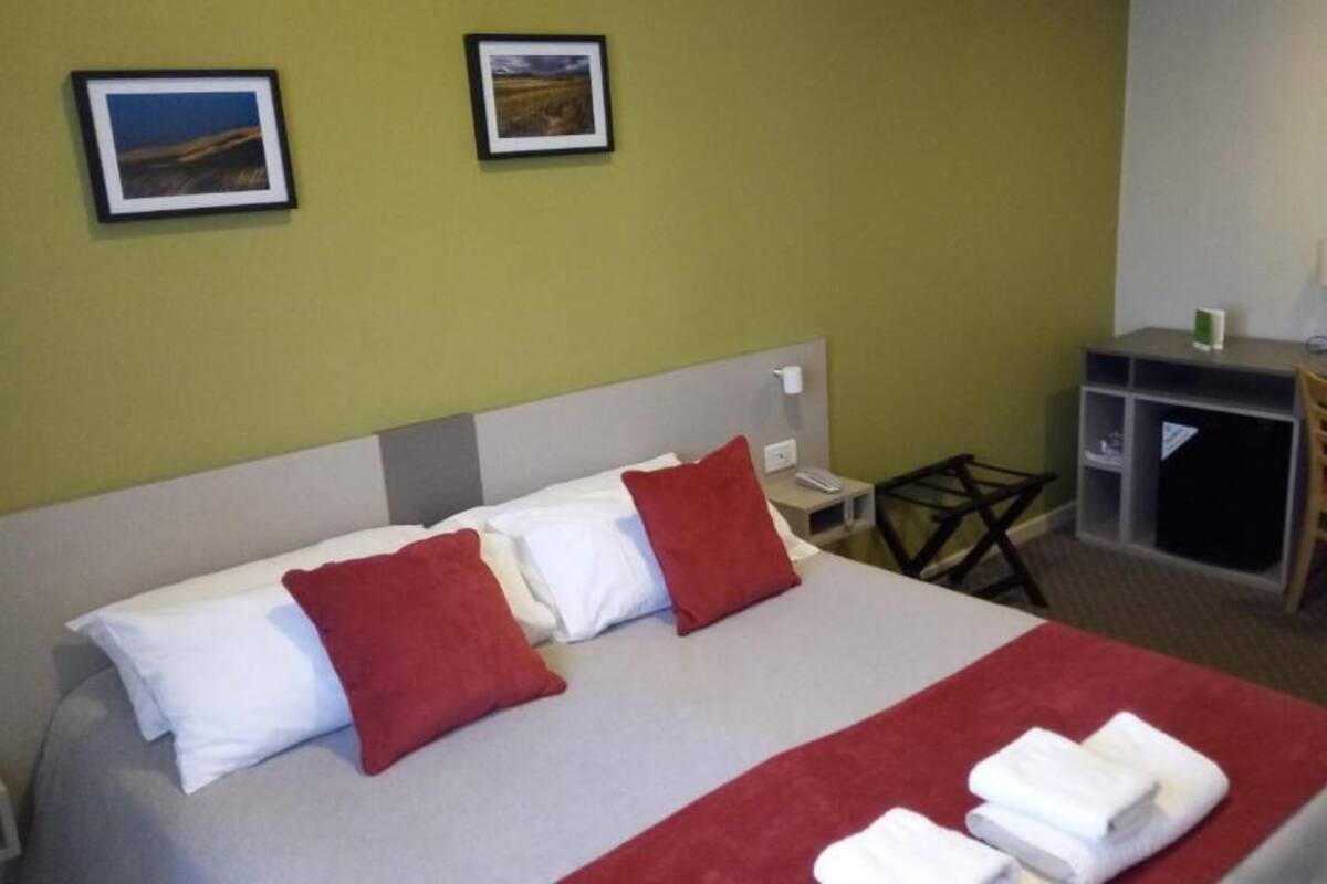 Une chambre d’hôtel avec un lit, deux oreillers, un bureau, une chaise et deux tableaux encadrés au mur.