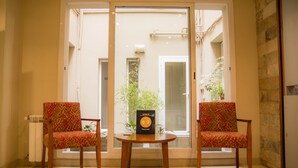 Une pièce avec deux chaises et une table, un radiateur et une fenêtre donnant sur un bâtiment et des plantes à l’extérieur.