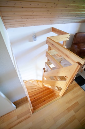 Una escalera de madera de diseño sencillo, un sillón de cuero marrón y una pared blanca con un enchufe.