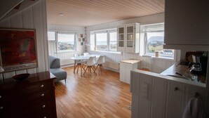 Een ruime keuken met houten vloeren, witte kasten en grote ramen met uitzicht op het landschap.