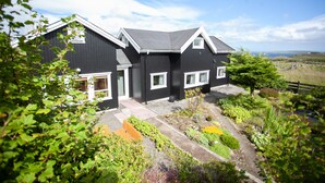Een modern herenhuis met twee verdiepingen, een zwart uiterlijk en witte details, omgeven door een verzorgde tuin en een mooi uitzicht over het landschap.