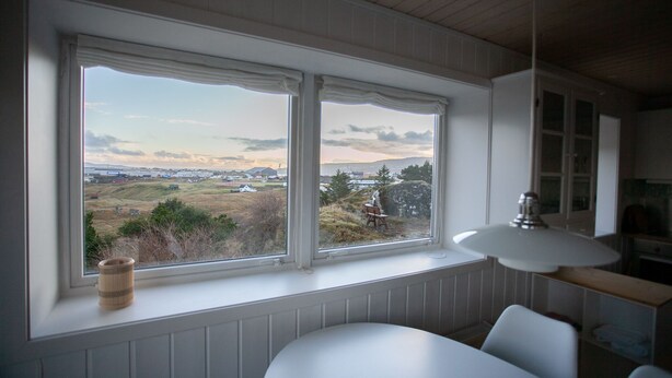 Een kamer met een groot raam met uitzicht op een landschap, een witte tafel en een lamp.