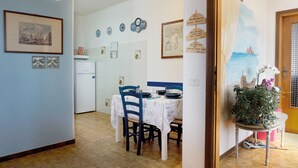 A dining area with a table set for four, a refrigerator, and various wall decorations including clocks and framed pictures. - Apartment in Villa Valentini, seafront, Gulf of Gaeta, parking included (Marina di Minturno)