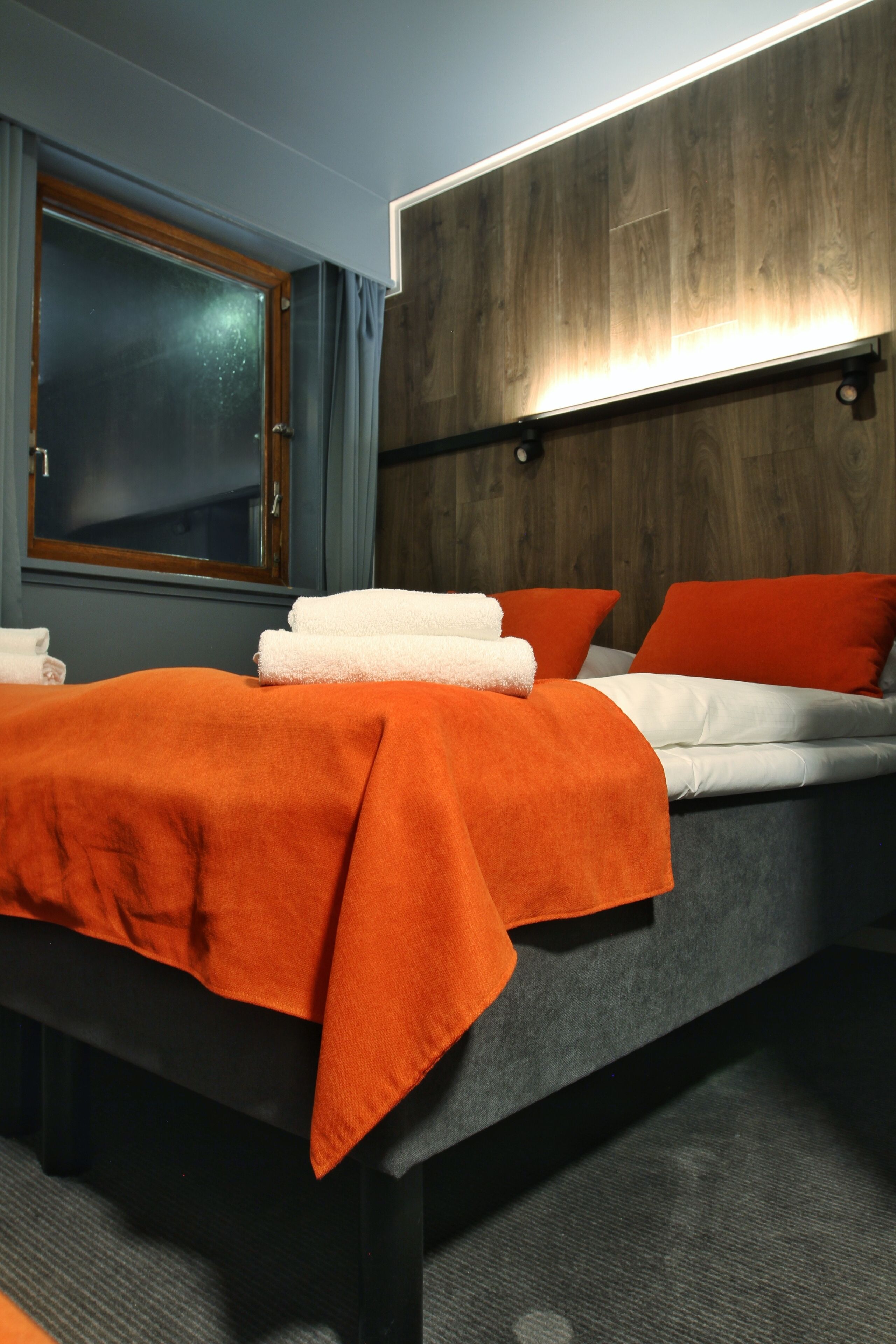 A hotel room with a bed, a window, and a wall-mounted light fixture.