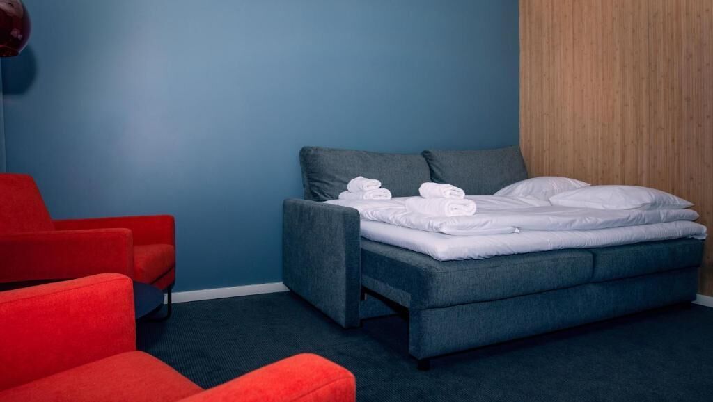 A modern hotel room with a blue wall, a grey sofa, and a bed with white linens.